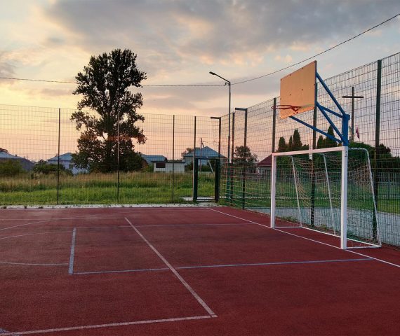 Outdoors mini football and basketball court with ball gate and basket surrounded with high protective fence.